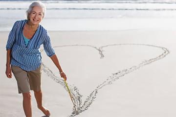 沙滩上的女人用棍子在沙滩上画一个心形